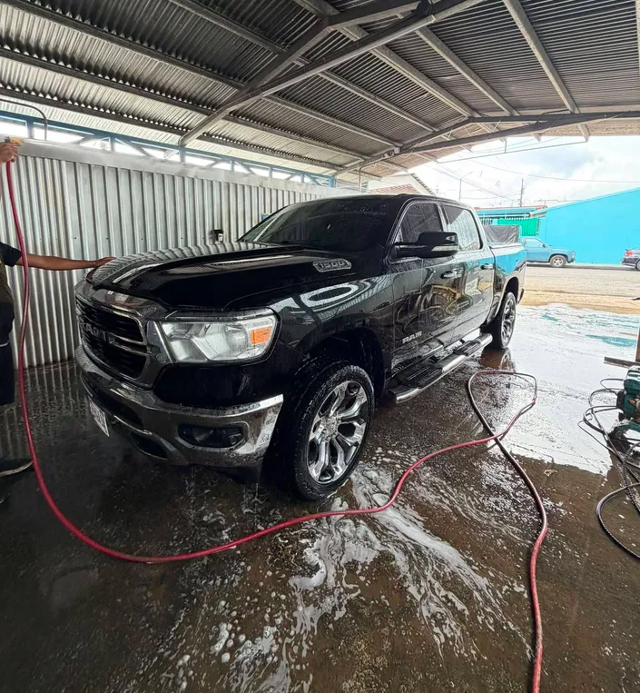 Una pickup RAM negra recién lavada, brillando bajo el techo del lavacar